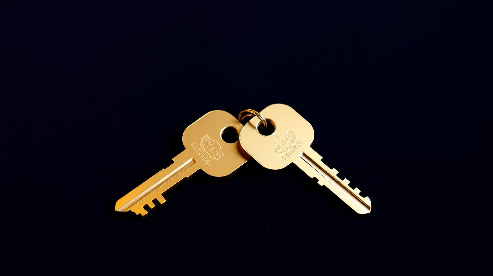 Two brass door keys side by side on a deep navy surface, identical in shape but slightly different in size