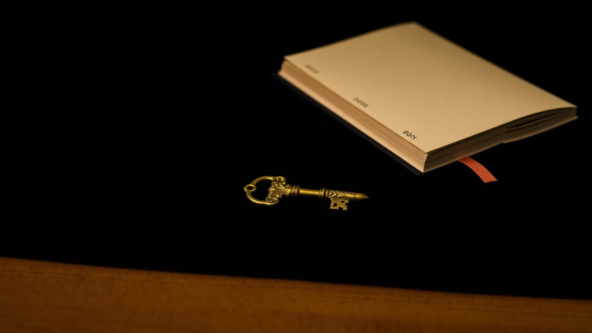 An ornate brass key resting on a deep navy surface beside a cream-paged ledger book
