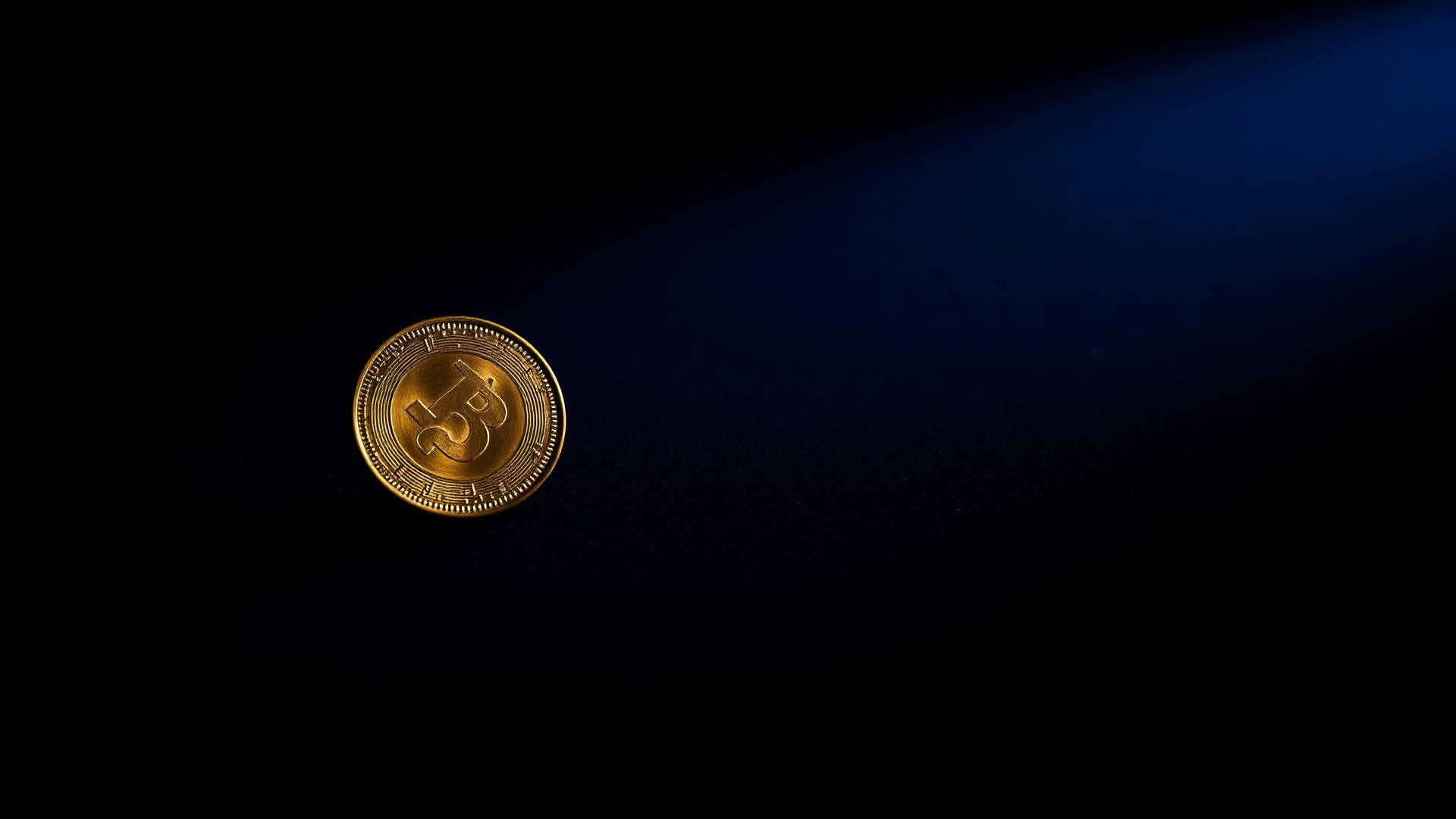 A single brass coin resting flat on a deep navy surface, lit from the side